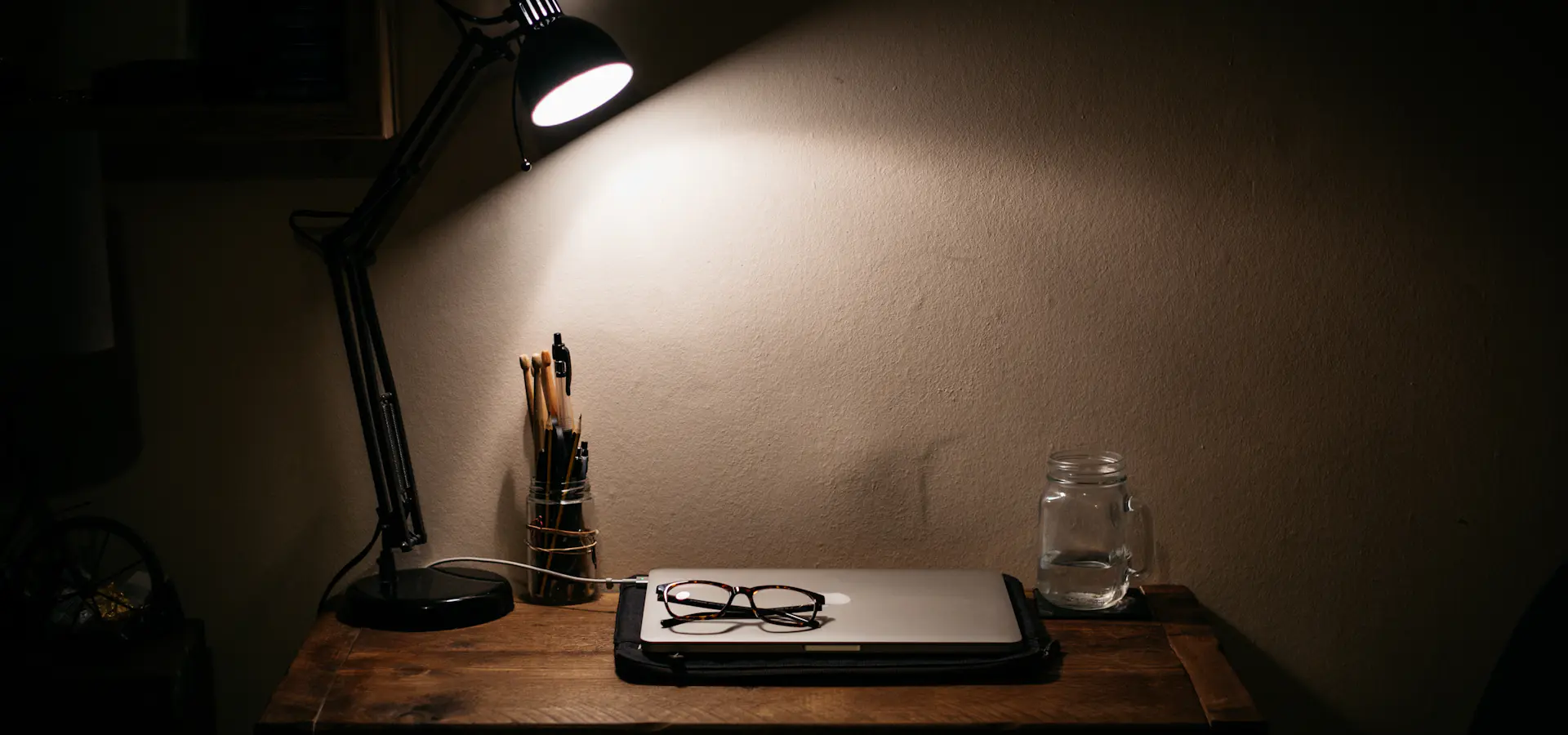 Wooden work desk with a lamp, a closed laptop and notes