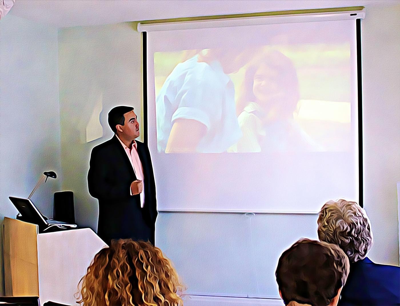Ignacio Segovia standing beside a projector screen while presenting to a seated audience